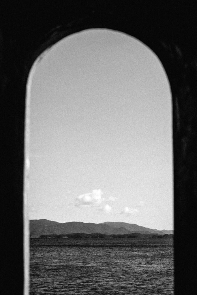 Black and white photo of the sea and mountains framed by an arched window.